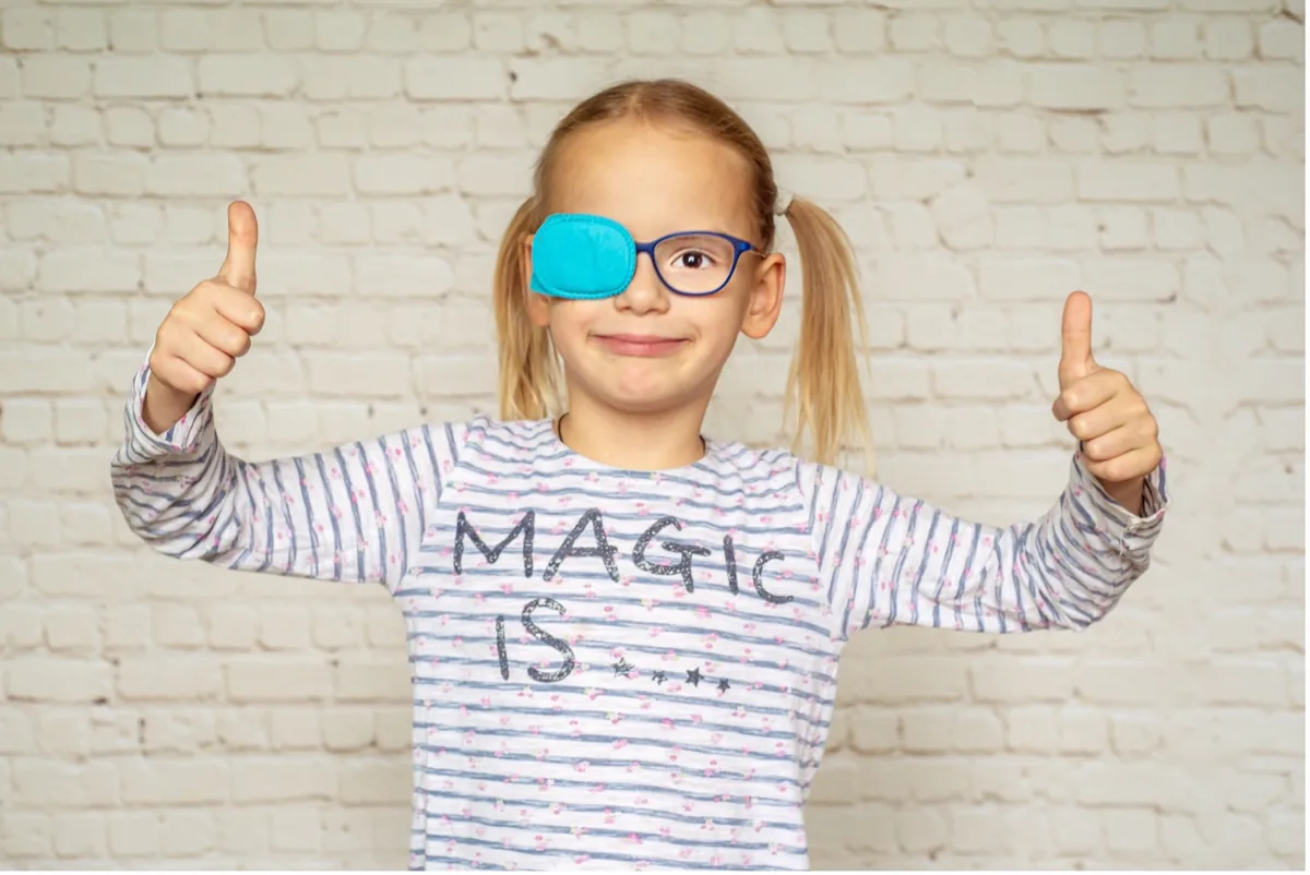 A young girl wearing an eye patch and giving a thumbs up